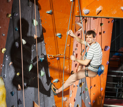 Climber young man climbing on practical wall indoor, looking to the camera