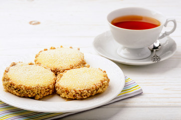 Butter cookies (alfajores) with caramel and peanut and cup of tea on wooden background.