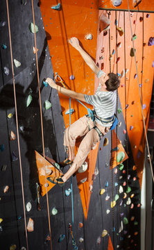 Athletic young male climber practicing rock-climbing on a rock wall indoors