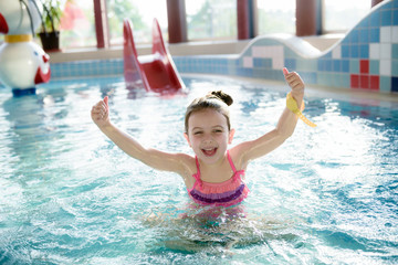 Naklejka premium Adorable little girl playing with water splashes at indoor pool 