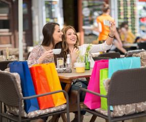 Two smiling female friends driniking coffee and taking selfie