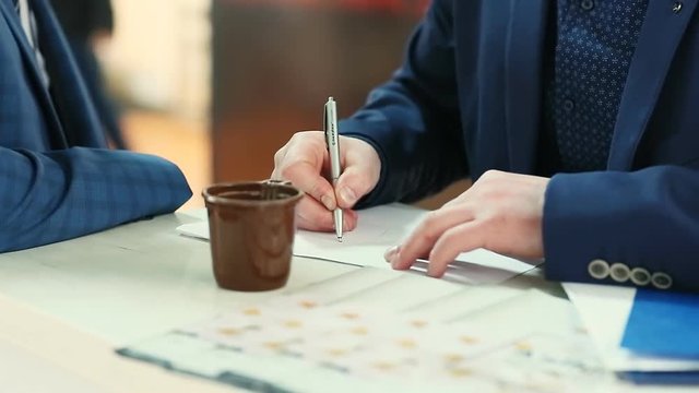 Businessman drawing business charts in copybook on desktop with office tools and coffee