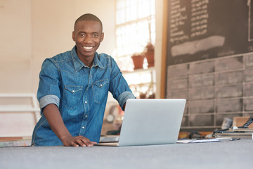 Smiling African design entrepreneur with his laptop in studio