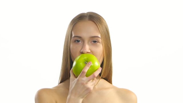 Young blonde model eating a big green apple and smile. White. Closeup