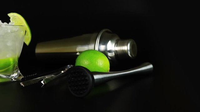 Caipirinha with cachaca, sugar and lime, bar tools on black background