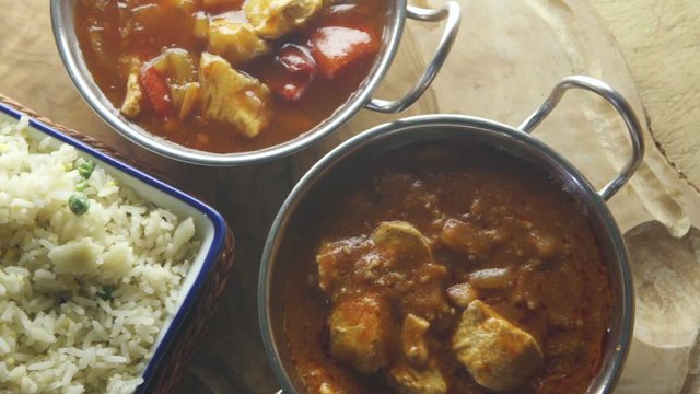 Ariel pan view of chicken and vegetable curry with rice. They are each in different dishes on a wooden board.