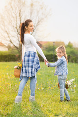 Fototapeta premium Beautiful young mother with her five years old daughter standing on the grass,and playing ,colored photo