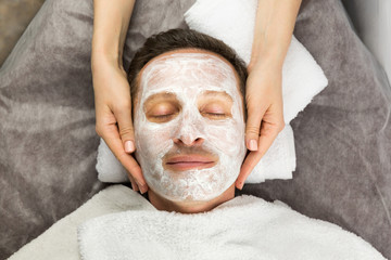 Face of man with cream mask and hands of professional cosmetolog