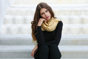 Closeup portrait of young beautiful brunette woman with wavy long hair stares into camera sitting on the concrete stairs