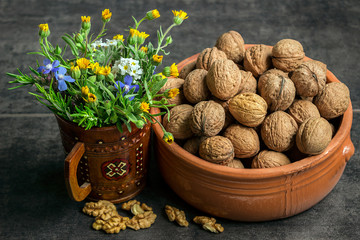 Walnuts in a ceramic pot on a dark background with a bouquet of wildflowers