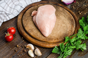 Fresh, raw chicken fillet, tomatoes, parsley, garlic on cutting board.
