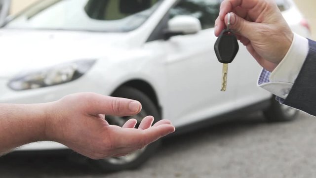 A man selling a car to another man and handing over the car key.