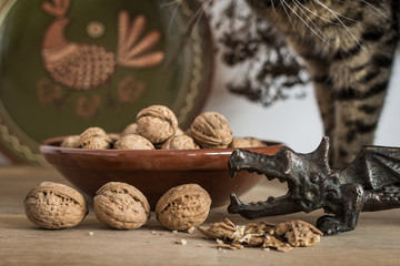 Dragon shaped nutcracker and some walnuts in cozy rustic kitchen with clay folk plates and tabby cat on wooden table.