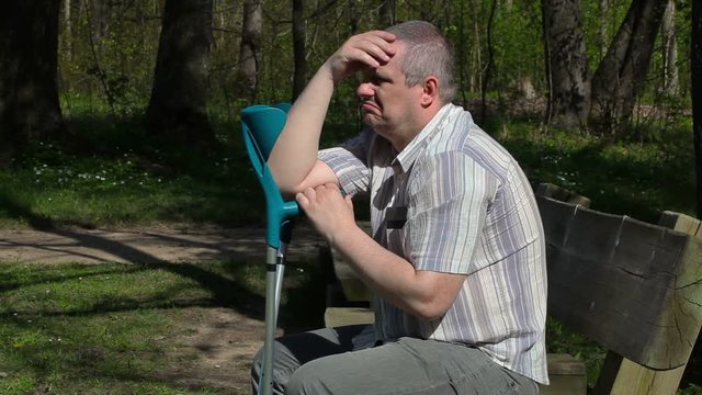 Disabled man with crutches thinking on bench in the park