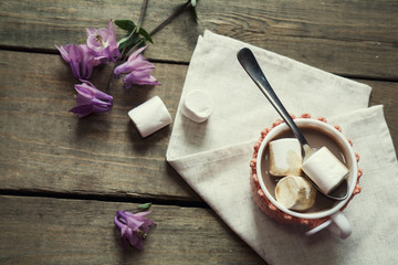 Hot cocoa with marshmallows in cup and cup crochet holder and fresh spring pink bell flowers on wooden table. Coloring and processing photos in vintage style with vintage selective focus.