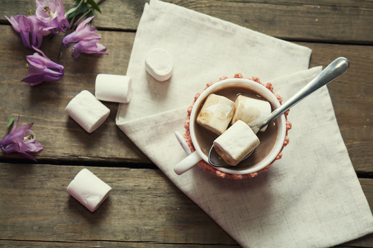 Hot cocoa with marshmallows in cup and cup crochet holder and fresh spring pink bell flowers on wooden table. Coloring and processing photos in vintage style with vintage selective focus.