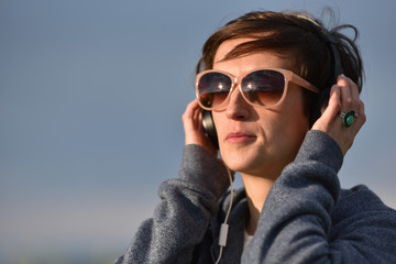 Young woman with sunglasses listening music in headphones in the