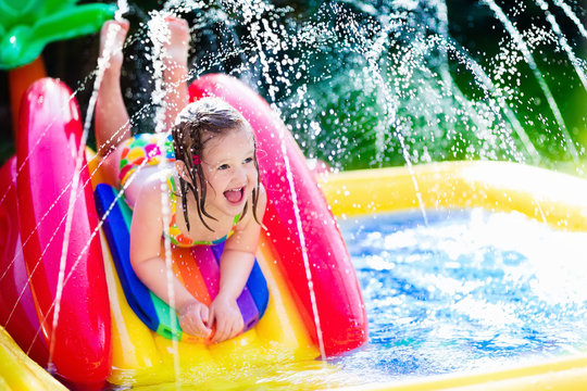 Little girl playing in inflatable garden swimming pool