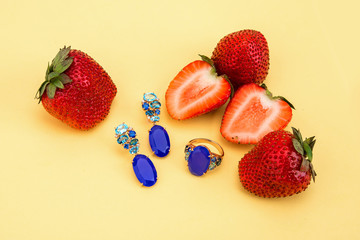 Different jewelries with topazes next to strawberry on yellow ba