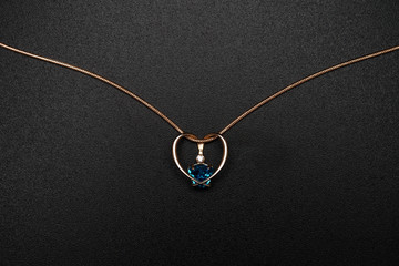 Fototapeta na wymiar Gold heart-shaped pendant with blue topaz on black background.
