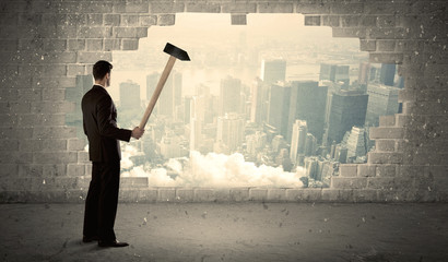 Business man hitting wall with hammer on city view