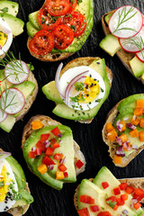 Avocado canapes  with various toppings on a black stone background