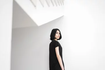 Calm black-haired woman looking at camera against of white wall © alexnope