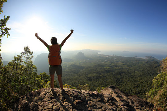 silhouette of young successful woman hiker open arms on mountain peak