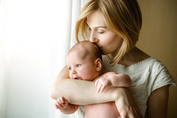 newborn baby in a tender embrace of mother at the window