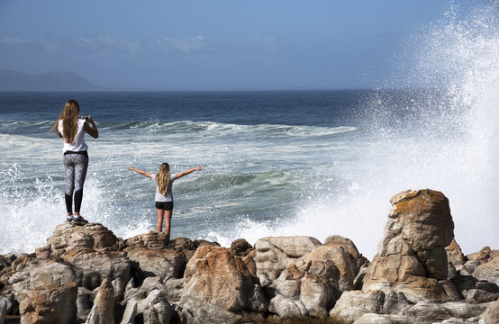 HERMANUS WESTERN CAPE SOUTH AFRICA - APRIL 2016 -  Young girls on rocks taking selfie photos as the Atlantic Ocean crashing below them at Hermanus Southern Africa