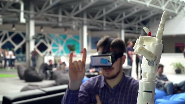 Cybernetic system today. Game industry and motion tracking in cyberspace. Man with innovative spectacles creates movement for mechanical plastic arm. Printing on the 3D printer. Sci Fi and prosthetics