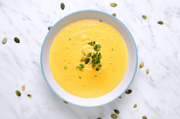 Pumpkin soup in a bowl with spoon on a marble and thyme