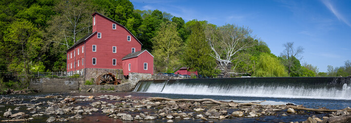 Naklejka premium Panoramic view of historic red mill building on river with dam