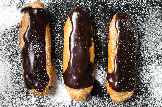 Eclairs with chocolate on a black background with powder
