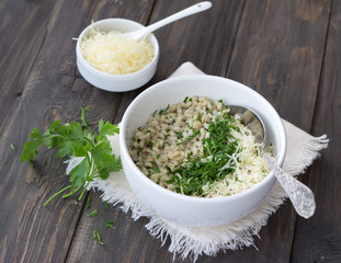 Pearl barley with cheese and herbs in white ceramic bowl on the wooden table. Delicious and healthy breakfast
