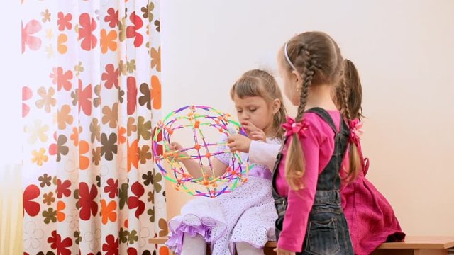 Cute little girls playing with educational toys sitting on a brench