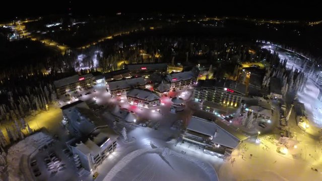 Aerial view of ski centre area at night. Illuminated hotels and slopes in the pinery. Winter recreation