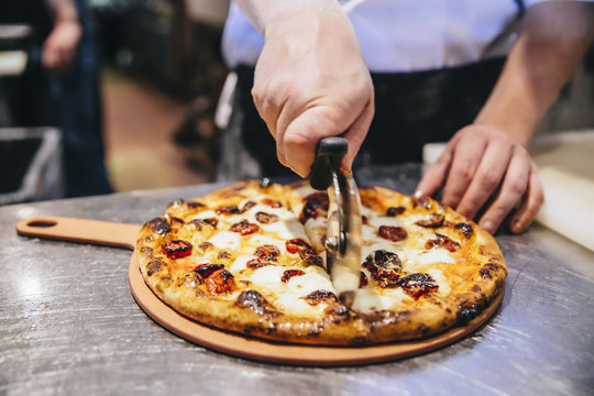 Chef making slices of pizza on pizza board in the restaurant kitchen
