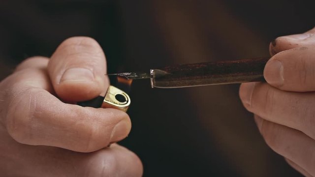 Man preparing pen for writting with a lighter. Calligraphy lesson. Close up. Slow motion