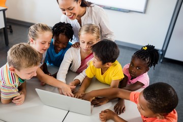 Happy teacher and pupils using laptop 