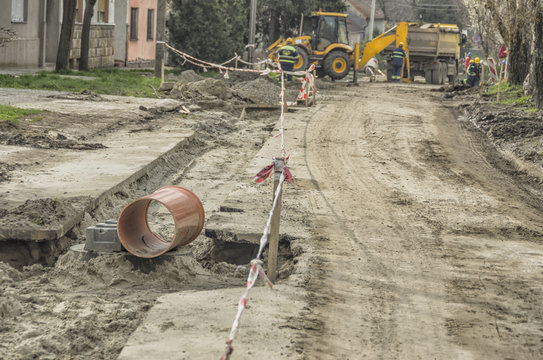 Sewage pipe waiting for installation at construction site in the street with workers and machinery in background