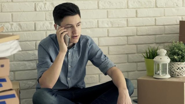Teenage boy talking on cellphone while sitting on floor at new home
