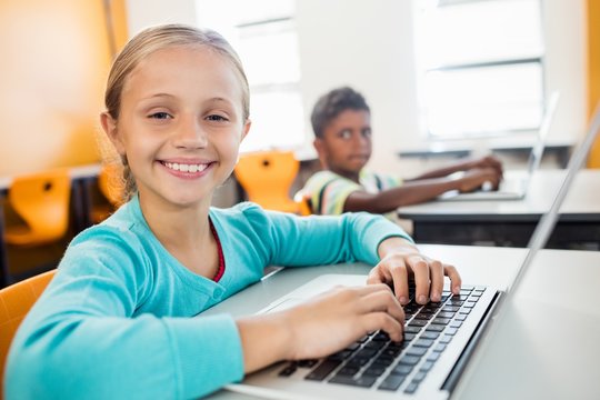 Smiling pupil posing with laptop at desk in classroom