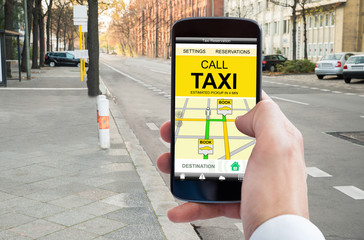 Person's Hand Booking Taxi On Smart Phone