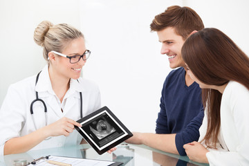 Doctor Showing Ultrasound Scan Of Baby To Happy Couple
