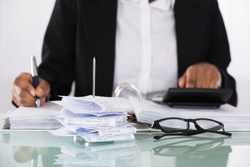 Close-up Of Businesswoman Calculating Tax On Desk