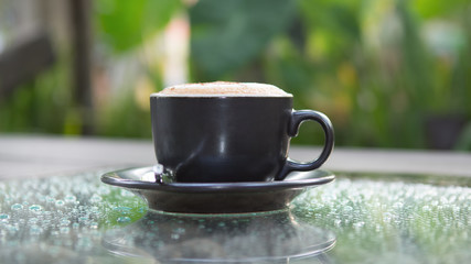 Hot cappuccino coffee cup on grass table in garden with dewdrop