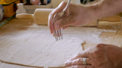 An attractive man poking a fork into dough while making home made matzo