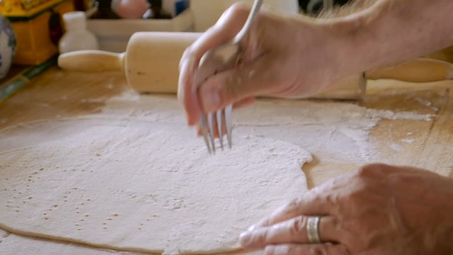 An attractive man poking a fork into dough while making home made matzo