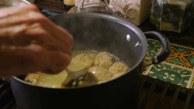 Close up of a man's hand stirring and cooking matzah ball soup on stovetop